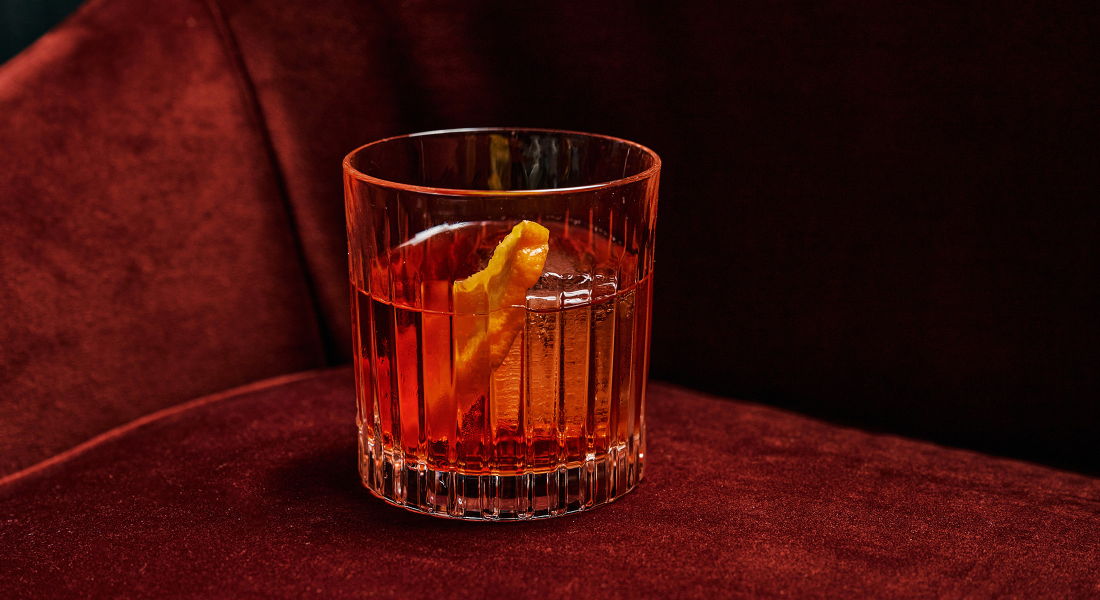 a red orange negroni with a lemon, swimming in ice, on a velvety surface